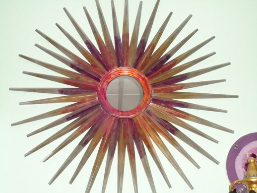 Espelho de parede redondo em formato de sol com moldura decorativa feita de múltiplos fios de metal que imitam raios solares radiantes.