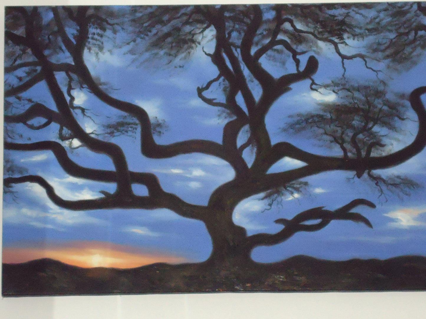 Quadro com pintura de uma árvore em silhueta negra ao centro sobre fundo de céu azul no crepúsculo com folhas no topo dos ramos.