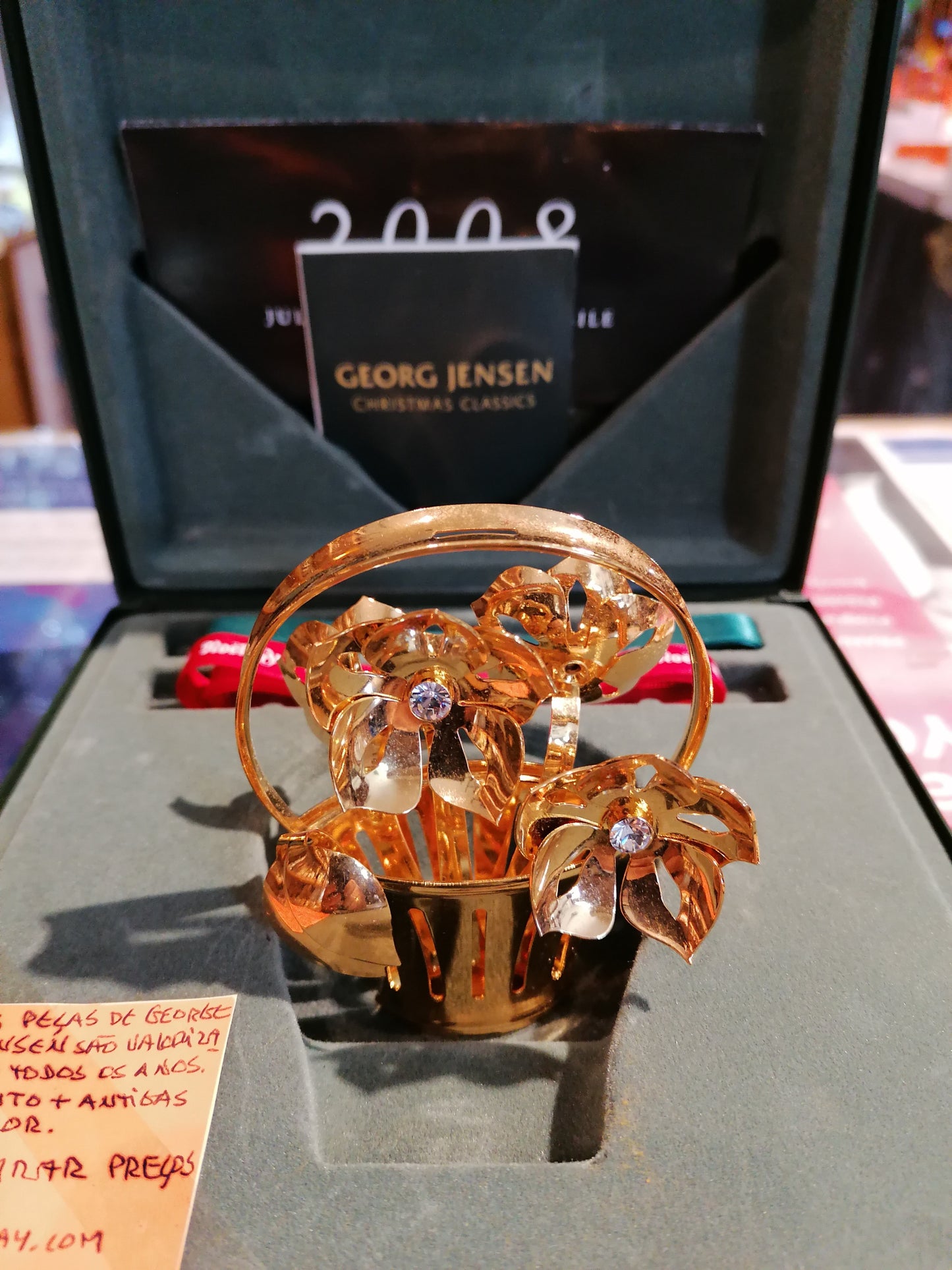 Ornamento de Natal Georg Jensen de dois mil e oito Christmas Rose banhado a ouro ao lado da sua caixa original vermelha.