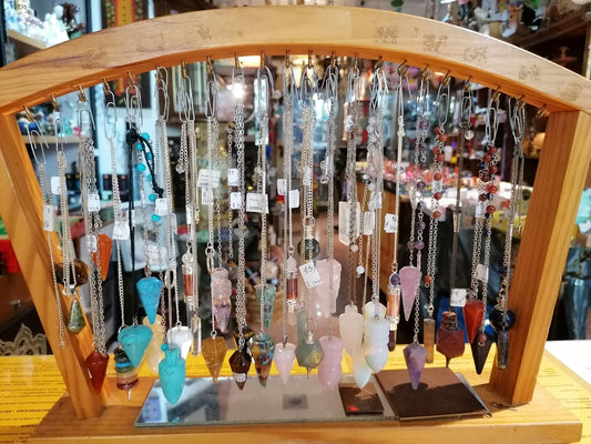 Coleção de pêndulos de radiestesia em cristal e metal sobre uma mesa de madeira.