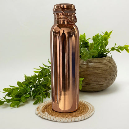 "Garrafa de água em cobre puro polido de 950ml, design Ayurvédico alcalinizante com pega prática. Garrafa artesanal elegante e saudável para hidratação diária."