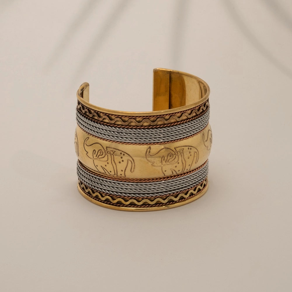 "Pulseira de braço artesanal em latão e cobre, com design em relevo de elefantes. Peça premium de estilo boho-chic com acabamento metálico misto."
