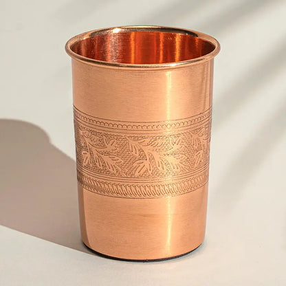 Copo de cobre puro artesanal de 300ml com gravura de flores na borda superior sobre fundo neutro.