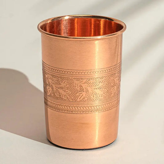 Copo de cobre puro artesanal de 300ml com gravura de flores na borda superior sobre fundo neutro.