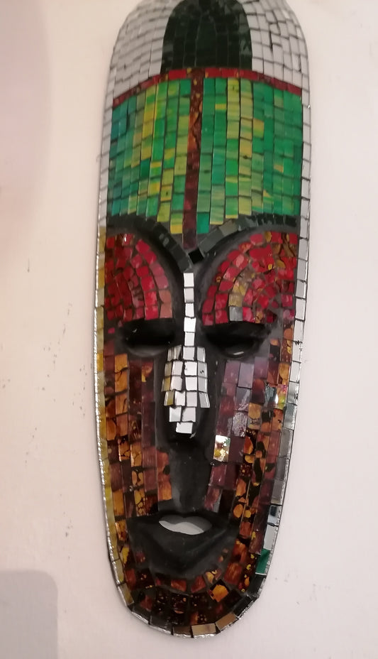 Máscara decorativa de rosto masculino grande forrada com mosaico de pequenos espelhos em tons de verde e vermelho refletindo a luz.