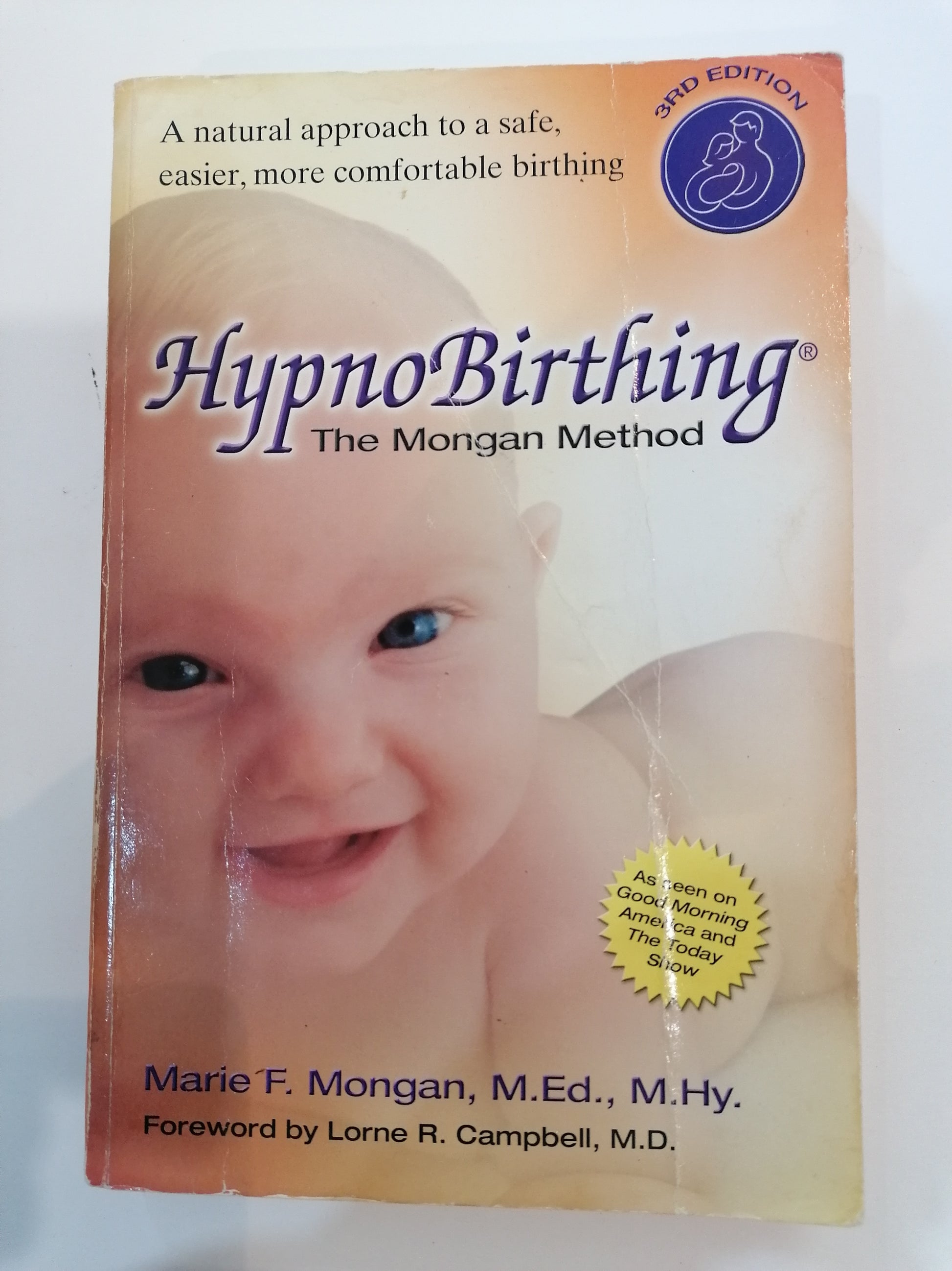  Livro The Mongan Method de Marie Mongan sobre parto natural, capa com tons relaxantes e foco em maternidade.