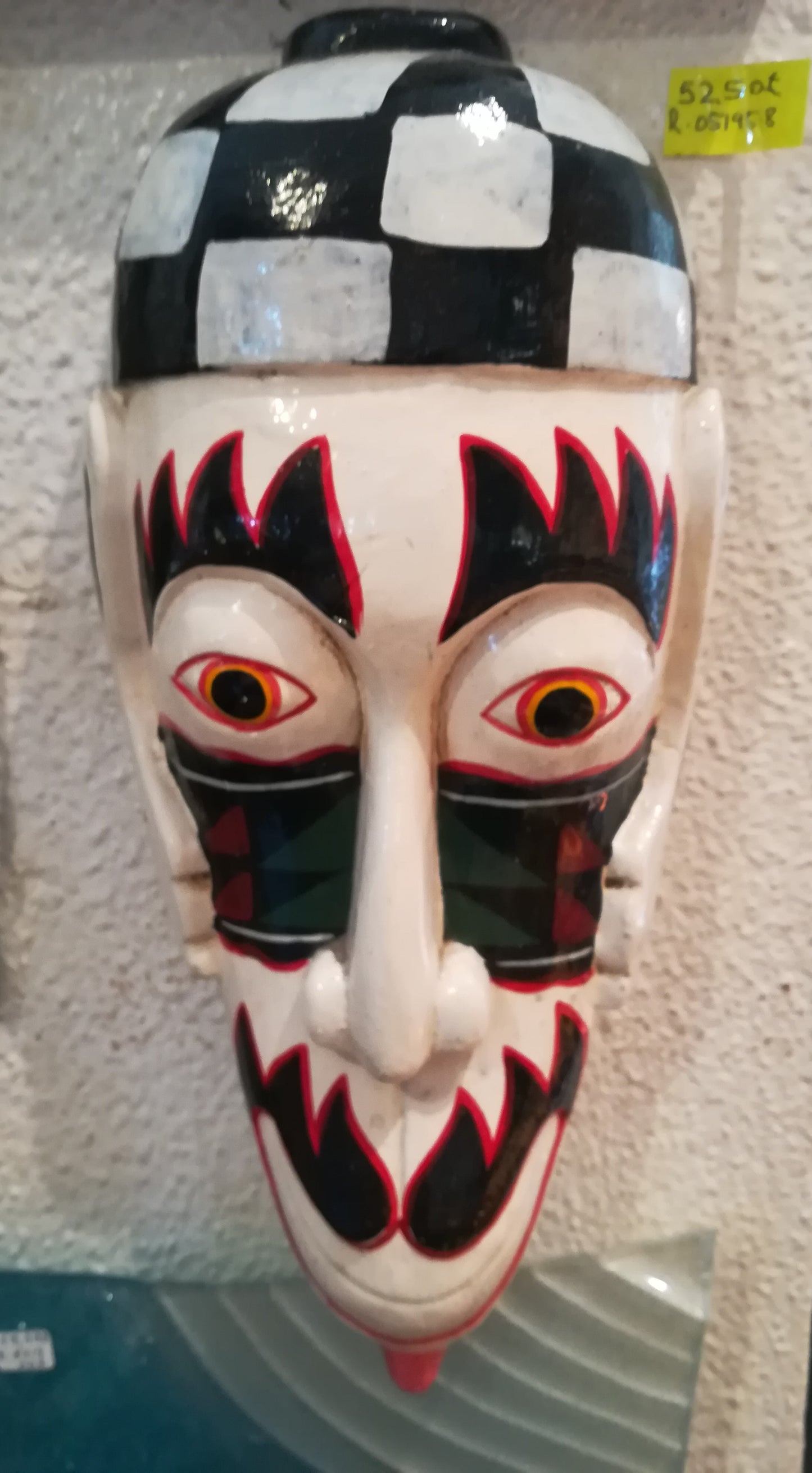 Máscara japonesa tradicional Kumadori de teatro Kabuki com padrão quadriculado, sobrancelhas e bigode de labaredas pretas e vermelhas sobre fundo branco.